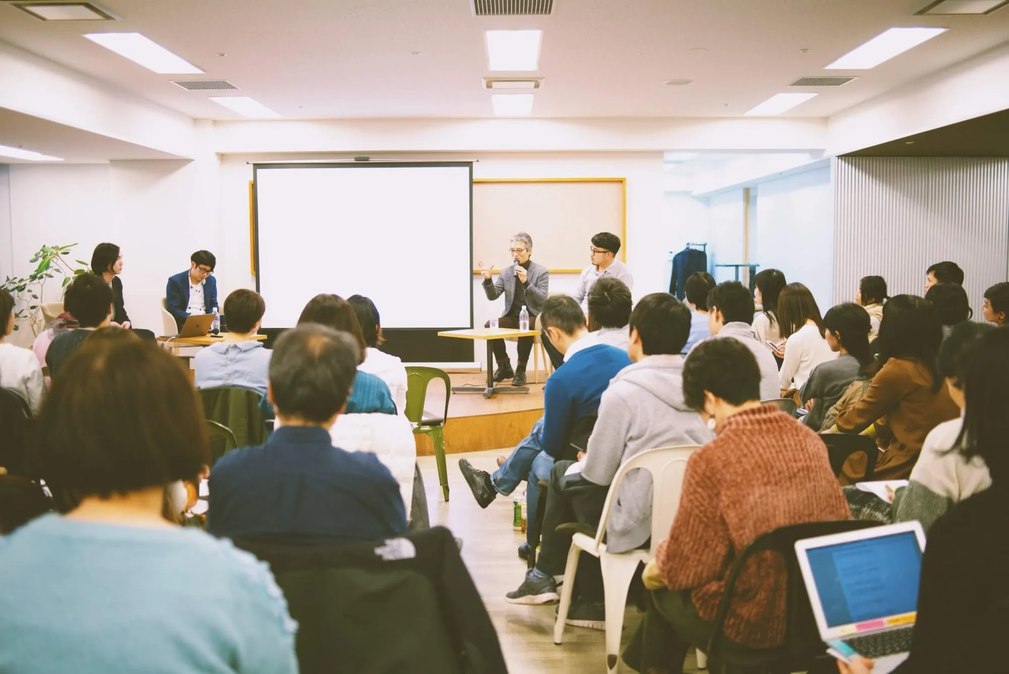 会場いっぱいの参加者の後ろから見た、前で話す登壇者